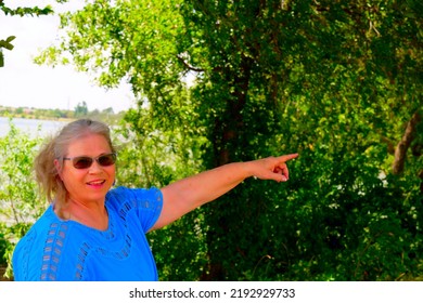 Mature Elderly Caucasian Woman Standing By A Tree And Pointing.