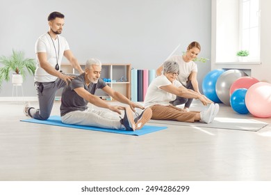 Mature elderly people doing stretching sport exercises with the help of fitness trainers sitting on yoga mat in rehabilitation center. Senior retired man and woman exercising for health in gym. - Powered by Shutterstock