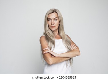 Mature Elderly Woman Standing Standing With Arms Folded Over Grey Background. Old Senior Female, 60s Gray-haired Lady Looking At Camera Arms Crossed, Portrait Close Up.