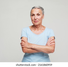 Mature Elderly Woman Standing Over Grey Background. Old Senior Female, 60s Gray-haired Lady Looking At Camera Arms Crossed, Portrait Close Up.