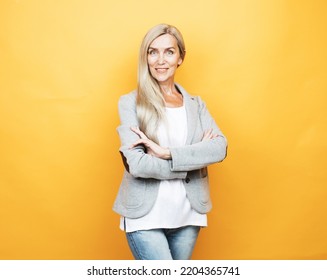 Mature Elderly Woman Standing Over Yellow Background. Old Senior Female, 60s Gray-haired Lady Looking At Camera Arms Crossed, Portrait Close Up.