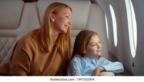 Mature Elegant Mother And Preteen Daughter Looking Through Window Flying On Airplane. Portrait Of Happy Mom And Little Daughter Enjoying Travelling In Business Class Cabin