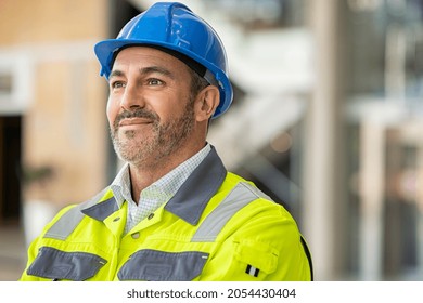 Mature engineer at construction site with safety vest and helmet looking away. Confident architect standing at site dreaming about finished project. Mature bricklayer thinking and day dreaming. - Shutterstock ID 2054430404