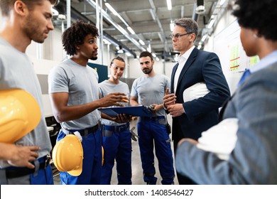 Mature Engineer Having A Meeting With His Employees And Communicating About Production Reports In A Factory.