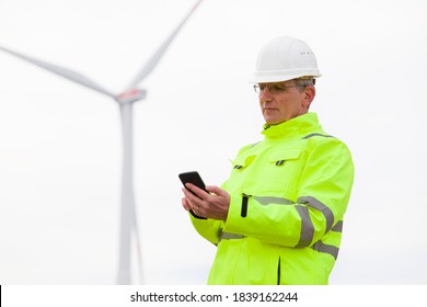Mature engineer looking at smart phone in front of a wind turbine - focus on  the face