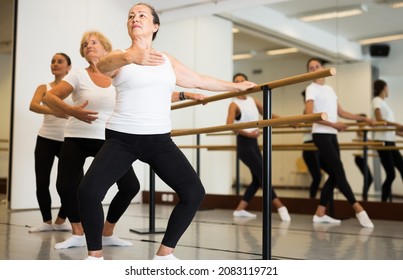 Mature European woman doing ballet at a group training session in the studio performs demi plie near the ballet barre, ..standing in a ballet stance