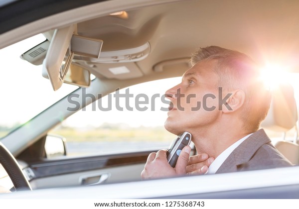 Mature executive\
trimming while looking at mirror in car with a lens flare\
highlighting the strong sun\
rays