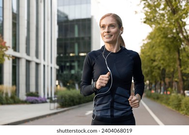 Mature experienced adult woman running in headphones in tracksuit outside modern building near trees, happy with workout sportswoman smiling active lifestyle. - Powered by Shutterstock