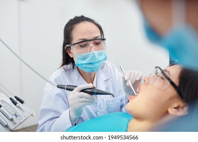 Mature Experienced Dentist In Goggles And Protective Mask Drilling Teeth Of Patient Suffering From Cavity