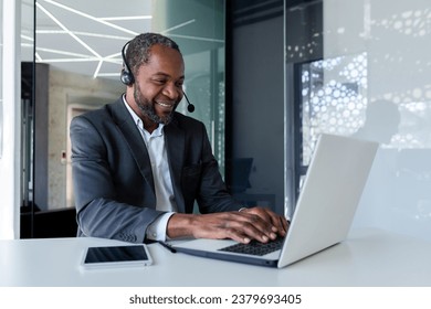 Mature experienced man in business suit with headset phone, working inside office with laptop, businessman online customer support worker, consulting customers remotely, selling in telestore. - Powered by Shutterstock