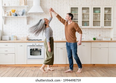 Mature family middle-aged couple wife and husband dancing together in the kitchen, celebrating date anniversary. Active seniors, love and relationship concept. Social distance.