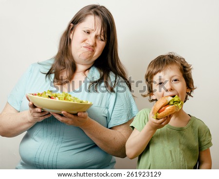 mature fat woman holding salad and little cute boy with hamburger teasing