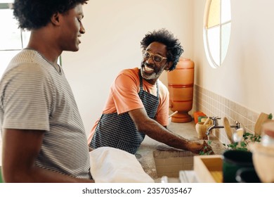 Mature father and his teenage son wash their hands at the sink in a Brazilian kitchen, using a clay filter for clean water. Happy family promoting cleanliness and hygiene in their home. - Powered by Shutterstock