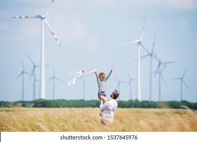 Mature father with small daughter standing on field on wind farm.