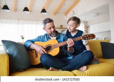 Mature father with small son sitting on sofa indoors, playing guitar. - Powered by Shutterstock