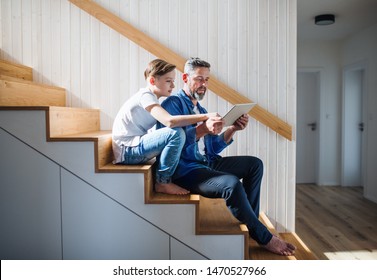 Mature father with small son sitting on the stairs indoors, using tablet.
