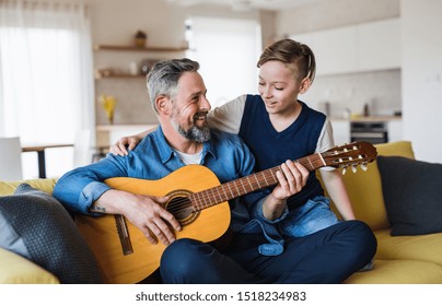 Mature father with small son sitting on sofa indoors, playing guitar. - Powered by Shutterstock