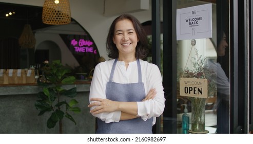 Mature female adult asia people open small bar pub look at camera enjoy laugh work with pride stand at modern SME store. Casual apron chef clerk staff in food or drink cafe coffee shop after pandemic.