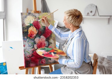 Mature female artist painting picture in  workshop - Powered by Shutterstock