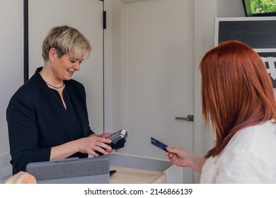 Mature female beautician charging for a service. Young beauty salon client paying for a service with her credit card. - Powered by Shutterstock