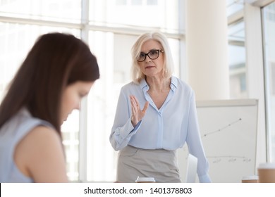 Mature female boss scolding young intern for bad work results at briefing, angry middle-aged businesswoman lecture, blaming employee, subordinate for business failure at company meeting, close up