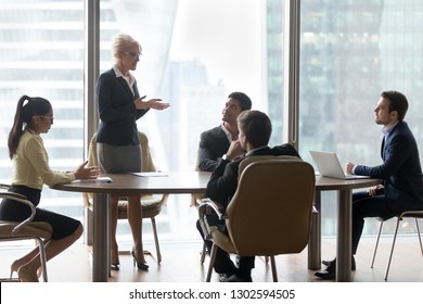 Mature Female Business Leader Coach Board Manager Speaking To Executive Team Explaining New Corporate Strategy At Group Meeting In Boardroom Training Employees In Modern Office Conference Table