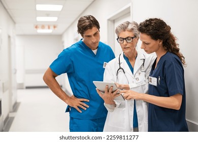 Mature female doctor discussing medical report with nurses in hospital hallway. Senior general practitioner discussing patient case status with group of medical staff after surgery. Doctors working. - Shutterstock ID 2259811277