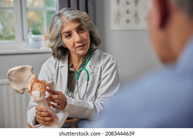 Mature Female Doctor Meeting With Male Patient Discussing Joint Pain In Hip Using Anatomical Model