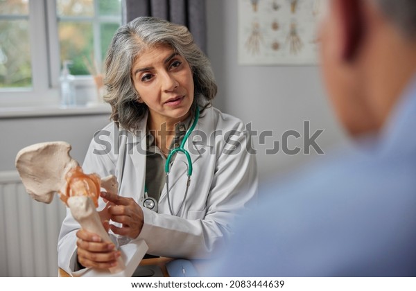 Mature Female Doctor Meeting\
With Male Patient Discussing Joint Pain In Hip Using Anatomical\
Model