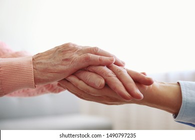 Mature female in elderly care facility gets help from hospital personnel nurse. Senior woman w/ aged wrinkled skin & care giver, hands close up. Grand mother everyday life. Background, copy space.