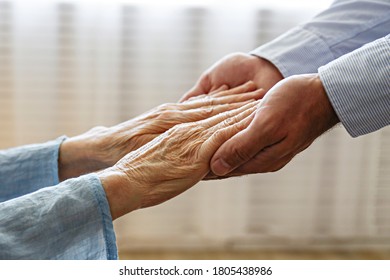 Mature Female In Elderly Care Facility Gets Help From Hospital Personnel Nurse. Close Up Of Aged Wrinkled Hands Of Senior Woman Reaching To A Male Doctor. Copy Space, Background