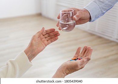 Mature female in elderly care facility gets help from hospital personnel nurse. Wrinkled hands of senior woman reaching to a male doctor handing her glass of water. Copy space, background, close up - Powered by Shutterstock