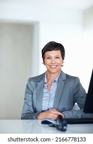 Mature Female Executive At Office Desk. Portrait Of Mature Female Executive Smiling At Office Desk.