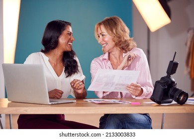 Mature Female Fashion Photographer With Assistant Looking At Brief For Fashion Shoot In Studio