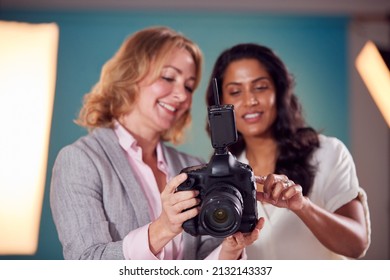 Mature Female Fashion Photographer With Client Looking At Images From Shoot On Camera In Studio