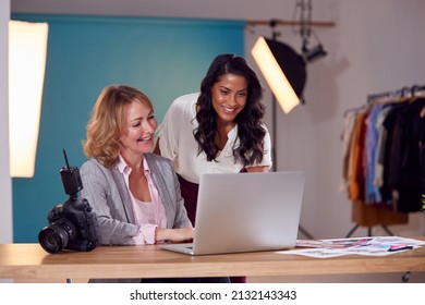 Mature Female Fashion Photographer With Client Looking At Images From Shoot On Laptop In Studio