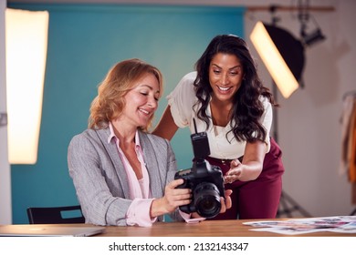 Mature Female Fashion Photographer With Client Looking At Images From Shoot On Camera In Studio