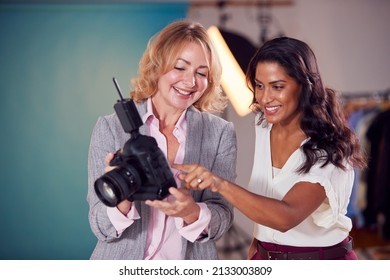 Mature Female Fashion Photographer With Client Looking At Images From Shoot On Camera In Studio