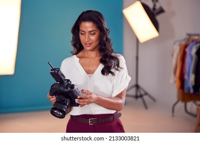 Mature Female Fashion Photographer Looking At Images From Shoot On Camera In Studio