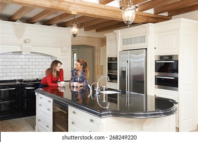 Mature Female Friends Standing In New Luxury Fitted Kitchen And Talking