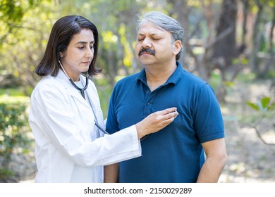 Mature Female Indian Doctor Wearing Apron Check Heatbeat Of Senior Male Patient With Stethoscope Outdoor In The Park, Healthcare, Illness.