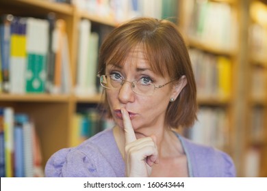 Mature Female Librarian Giving A Sign To Be Quiet Standing In Library Looking At Camera