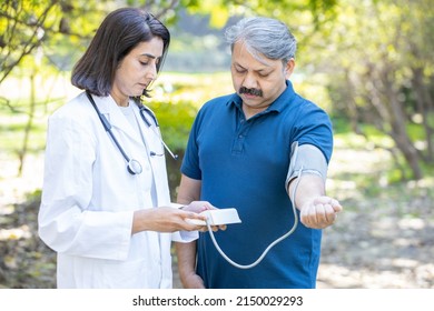 Mature Female Nurse Measure High Blood Pressure Of Sick Mature Male Patient In The Park, Woman Doctor Examine Do Checkup Of Man Client Heart Rate With Pulsimeter Monitor Outdoor.