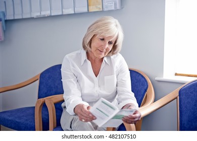 Mature Female Patient Reading Leaflet In Hospital Waiting Room