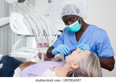 Mature female patient sitting in dental chair. Dentist is treating female patient - Powered by Shutterstock