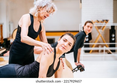 Mature Female Pilates Instructor Assisting Student On High-low Chair During Class In Exercise Studio.