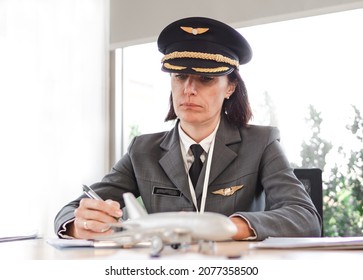 Mature female pilot sitting at desk thoughtfully look at aircraft model writing notes on paper. Smart woman airplane captain flight instructor preparing for training or meeting aviation business ideas - Powered by Shutterstock