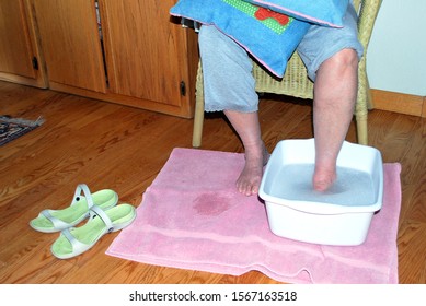 Mature Female Soaking Her Tired Feet In A Salt Bath Water Solution After Standing On Her Feet At Work All Day.