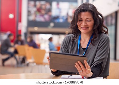 Mature Female Teacher Or Student With Digital Tablet Working At Table In College Hall