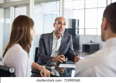 Mature financial agent showing new investment to young couple. Happy financial advisor discussing with a couple their mortgage loan. Happy couple consulting their bank agent about savings plan.